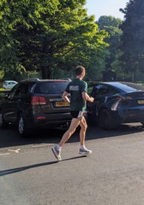 A man in a green tshirt runs to the right in front of two cars