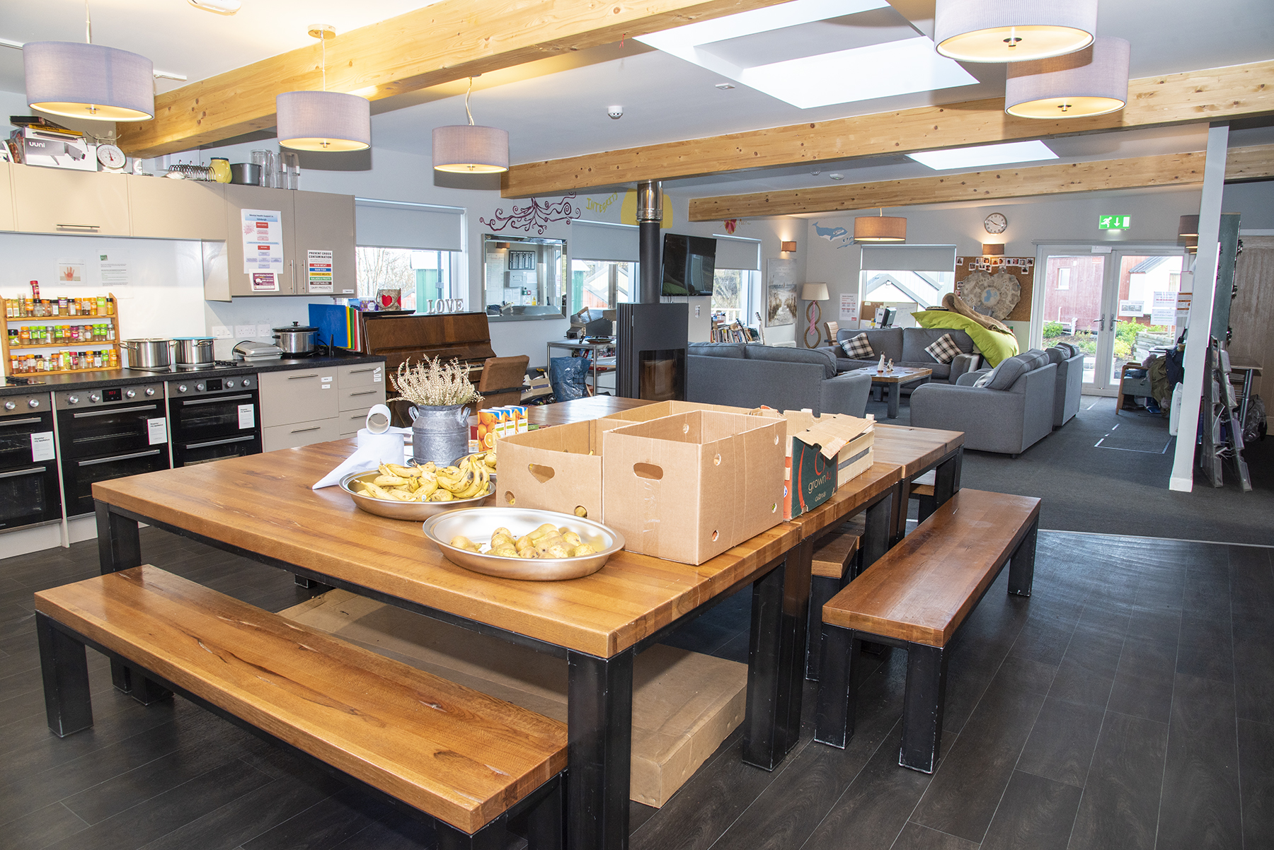 A huge communal kitchen dining table with boxes and snacks on it, looking on to a living room