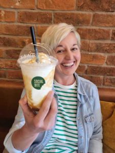 A woman smiles holding a clear plastic cup filled with a milkshake