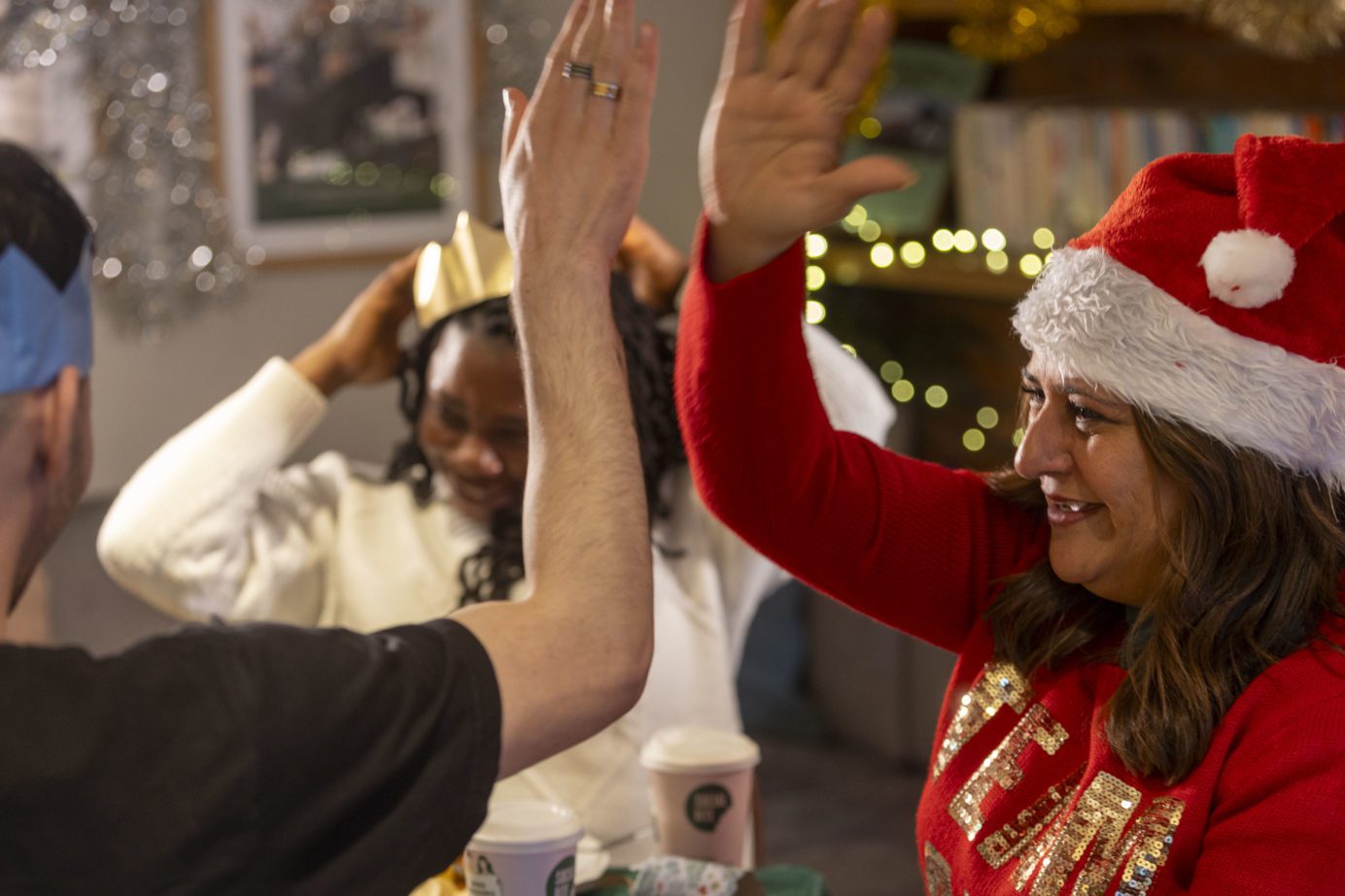 A woman in a Santa hat and a red jumper high-fives a man in a black tshirt